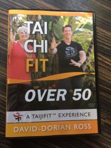 Over 50 woman and male instructor doing a Tai Chi movement with trees in background