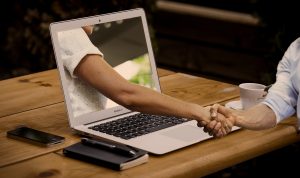 persons arm streching through a computer screen to shake hands and help