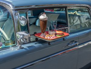 car with fast food attached on a tray at a drive in